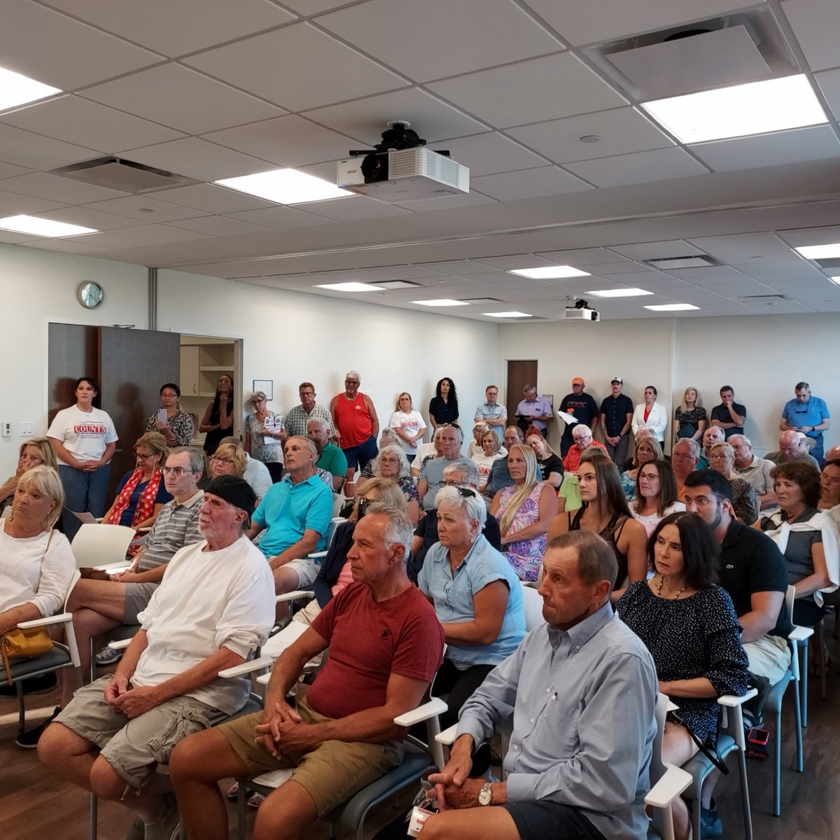 A full room at a club meeting, members standing at the back
